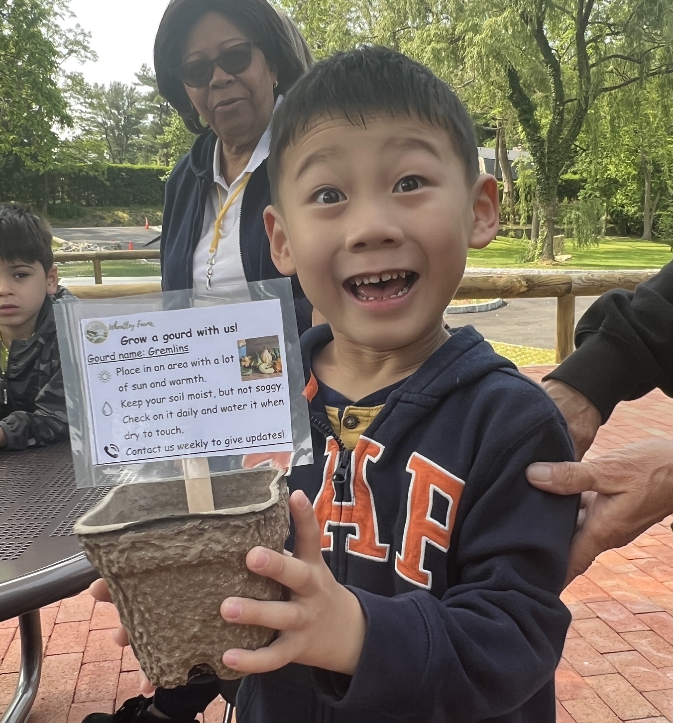 A child smiling while holding a planting pot with a sign sticking out from it with the words 