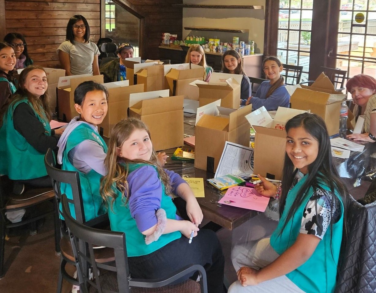 Troop 3322 and AHRC Nassau volunteers sitting at a table packing meal kits